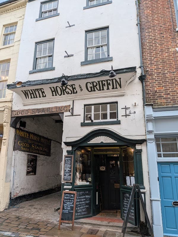 Historic building with a sign reading "White Horse & Griffin," featuring a welcoming entrance and cobblestone street.