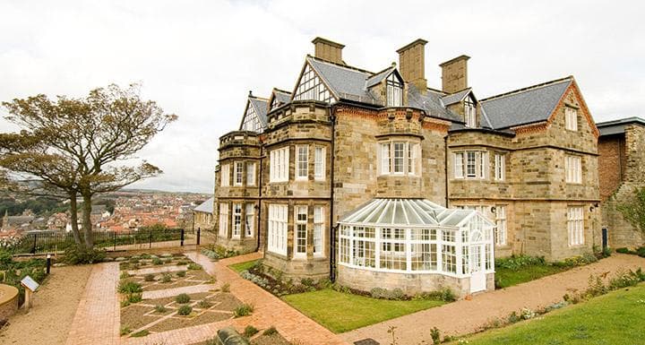 Victorian-style hotel with a glass conservatory, surrounded by gardens and overlooking a scenic view of Whitby.