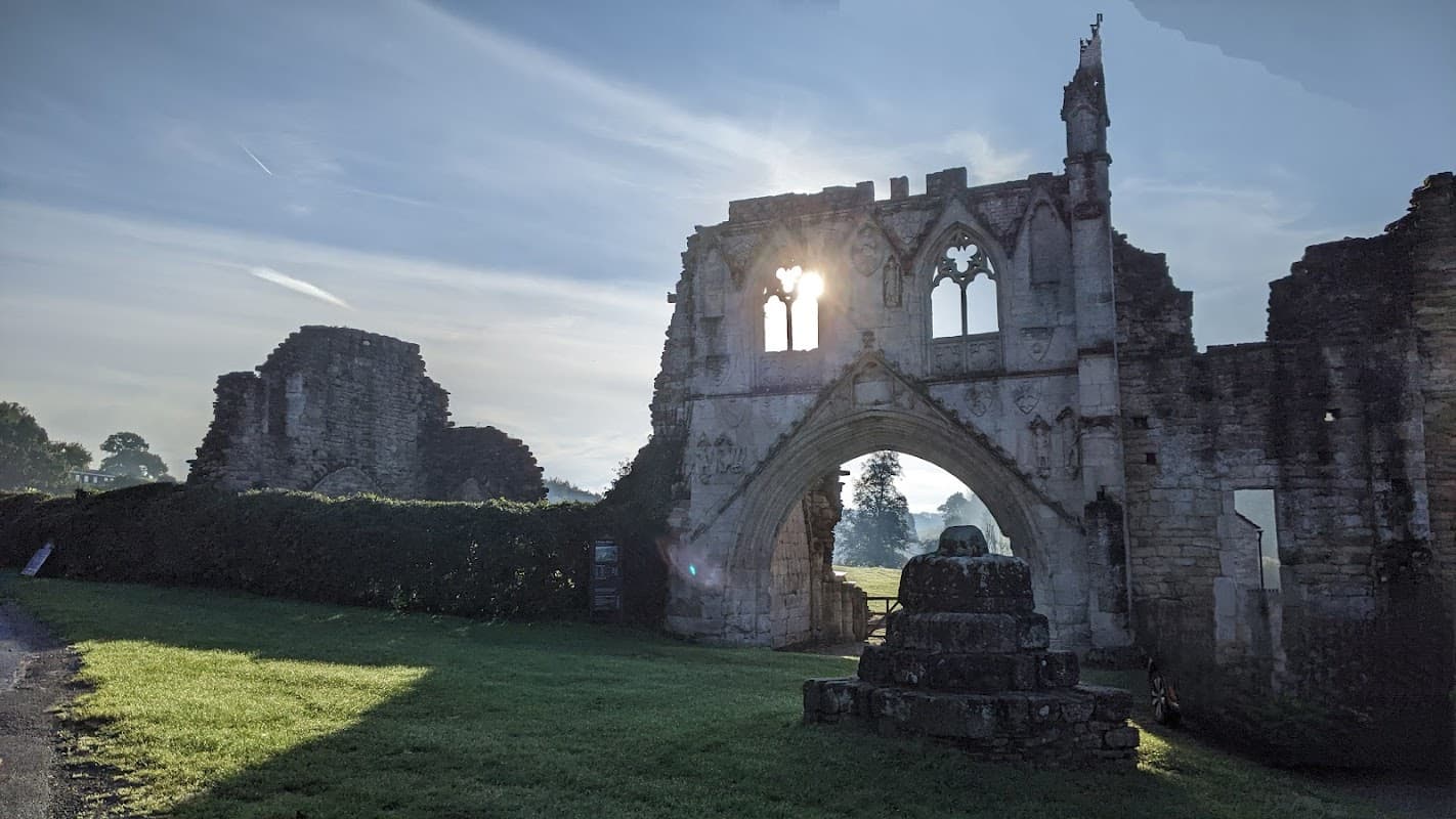 Ruins of an old structure with archways, surrounded by green grass and trees under a bright sky.