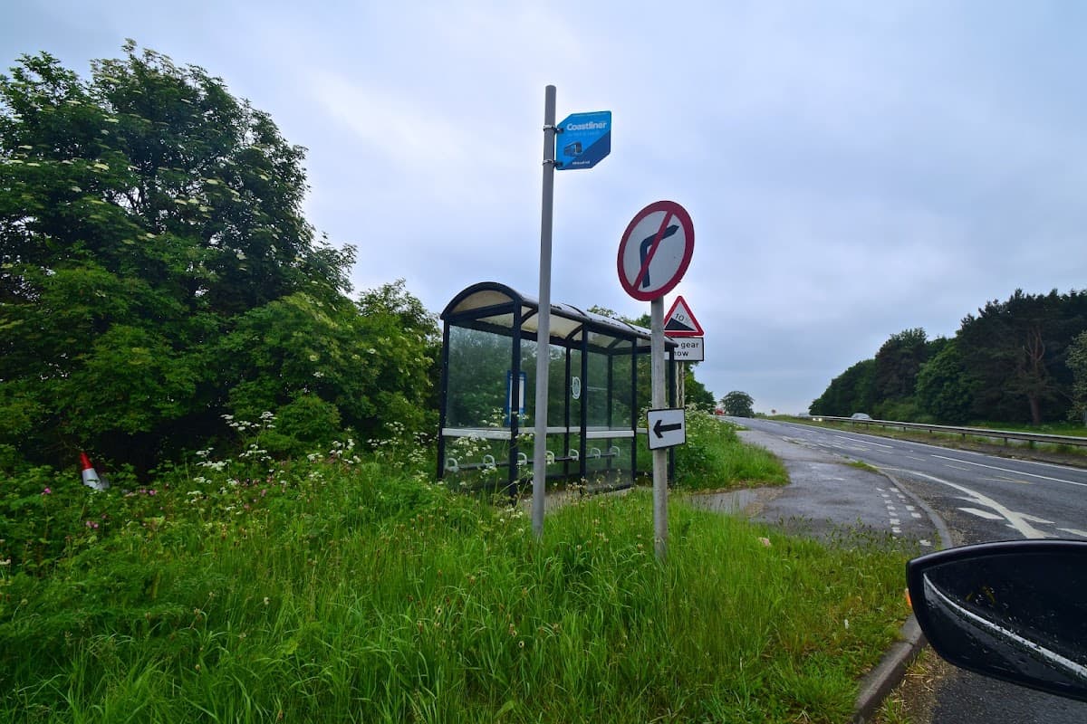 Bus stop shelter beside a road, with directional signs and lush greenery in Whitwell Hill, Yorkshire.