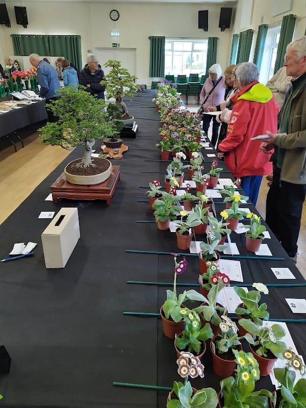 Indoor event at Wigginton Recreation Hall featuring attendees admiring potted plants and bonsai trees on display tables.