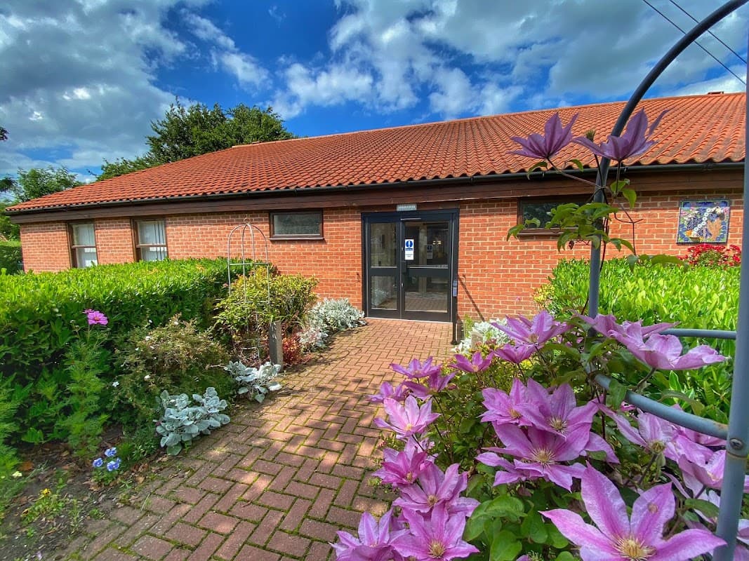 Wilberfoss Community Centre entrance surrounded by colorful flowers and greenery under a partly cloudy sky.