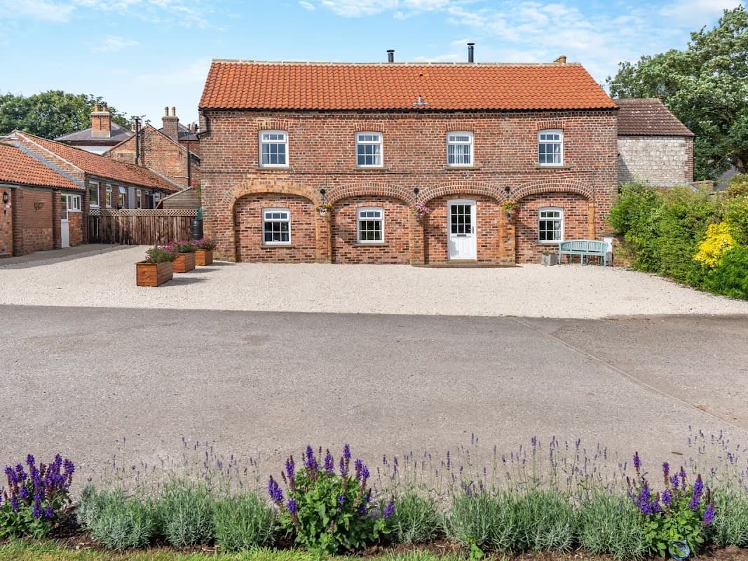 Brick farmhouse with a red-tiled roof, surrounded by gravel, planters, and a flower bed in Willerby, North Yorkshire.