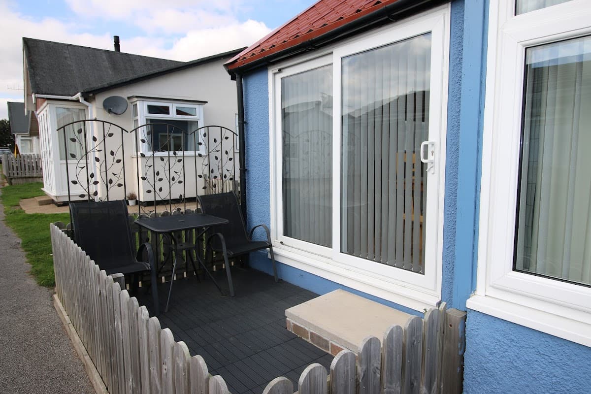 Blue holiday chalet with a patio, black chairs, and a small table, surrounded by a wooden fence in Wilsthorpe.