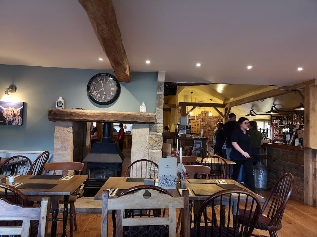 Cozy interior of The Barn with wooden beams, a clock, tables, and patrons at the bar in Winksley, Yorkshire.