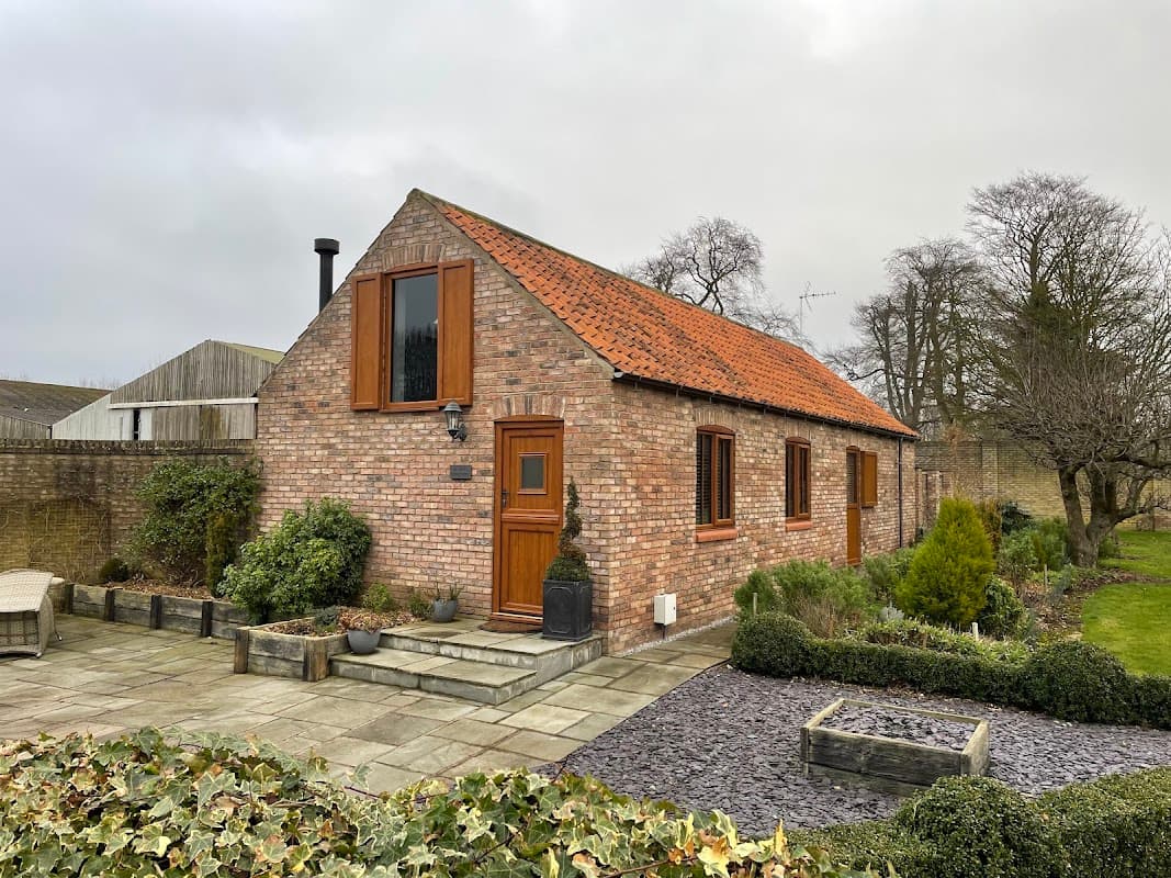 Charming brick cottage with a red-tiled roof, surrounded by greenery and stone pathways in Wold Newton, Yorkshire.