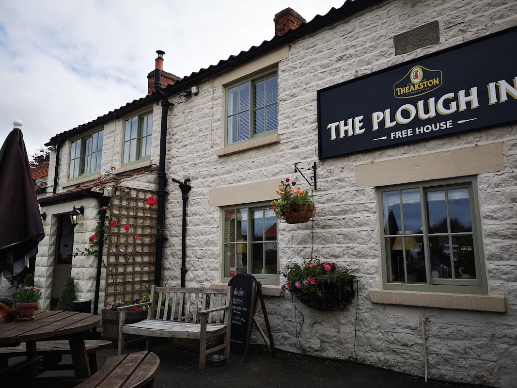 Charming pub exterior with stone walls, hanging flower baskets, and outdoor seating in Wombleton, Yorkshire.