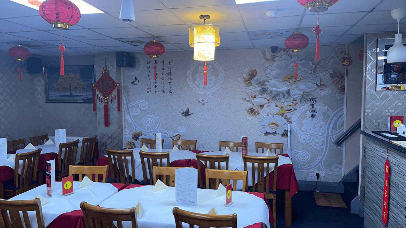 Interior of China Lantern restaurant with wooden tables, red tablecloths, decorative lanterns, and floral wallpaper.