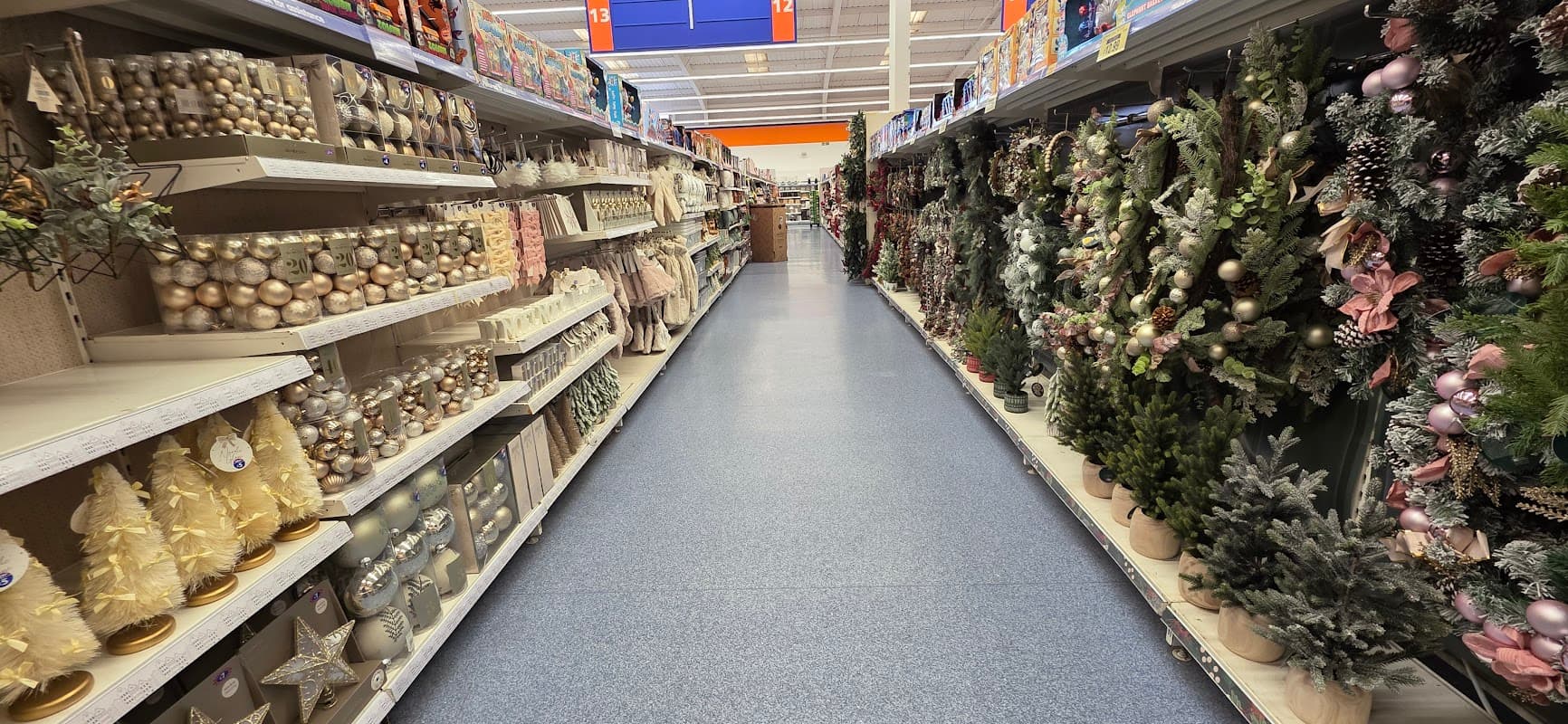 A brightly lit retail aisle filled with festive decorations, including trees, ornaments, and garlands on both sides.