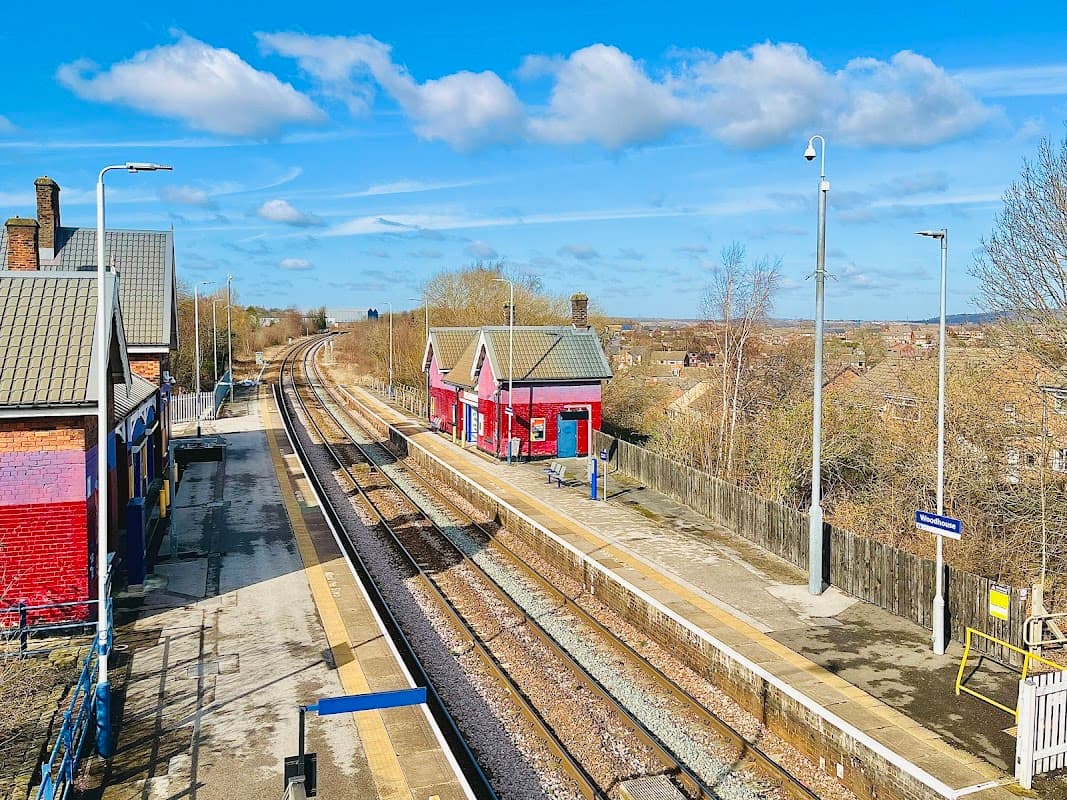 Two red railway buildings alongside empty platforms and tracks under a blue sky with scattered clouds.