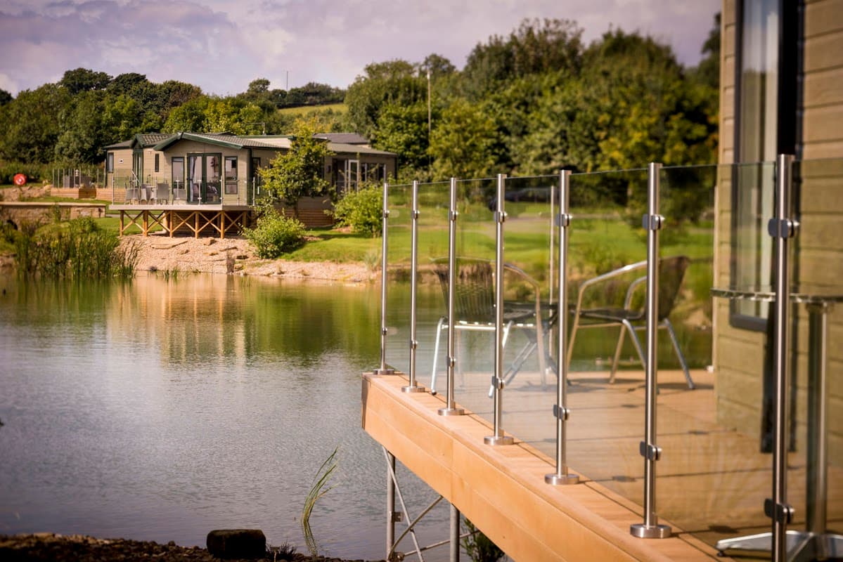 Lakeside view at Wayside Holiday Park with modern lodges and glass railings, surrounded by greenery in Yorkshire.