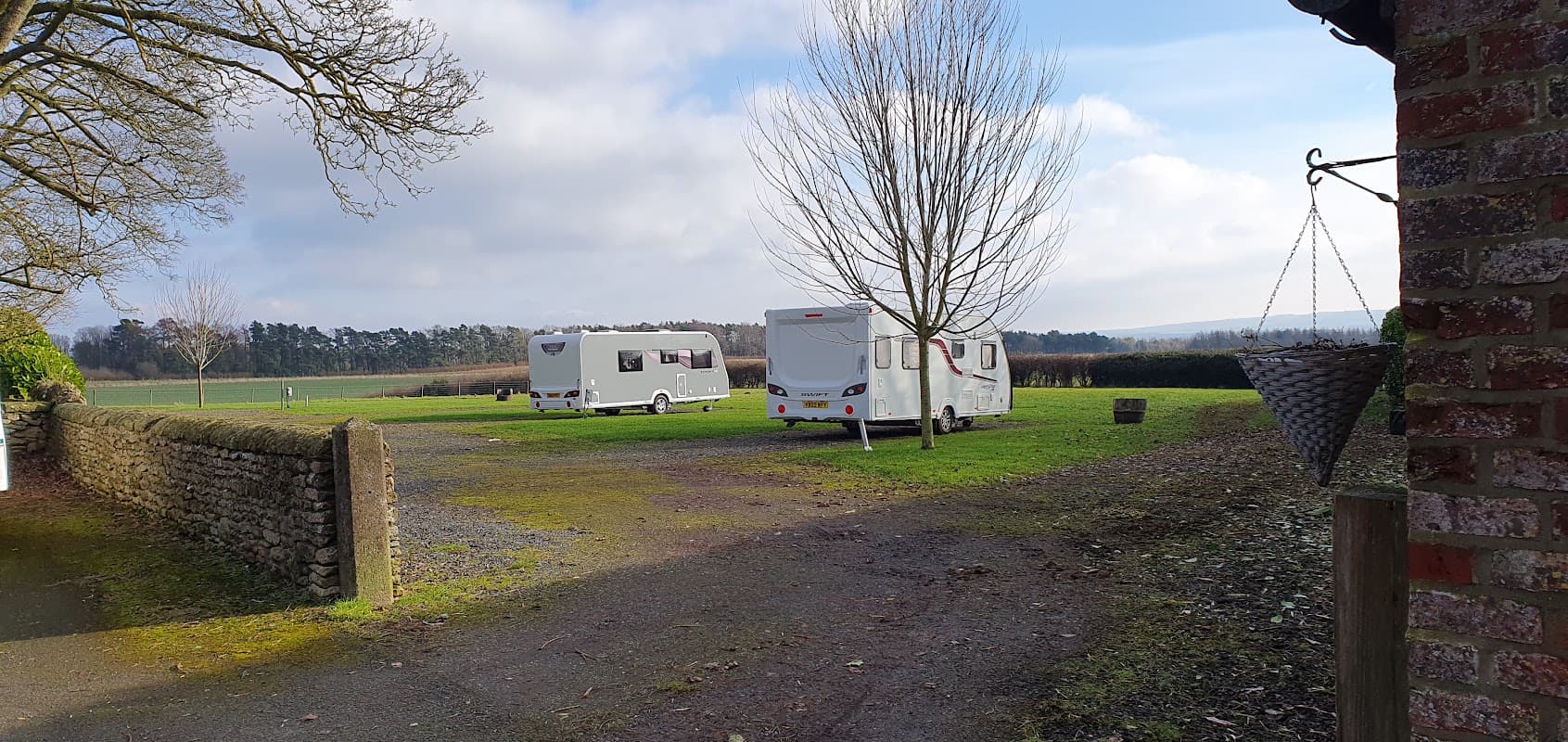 Two caravans parked on grassy area at Wykeham Grange Farm, surrounded by trees and open fields under a cloudy sky.