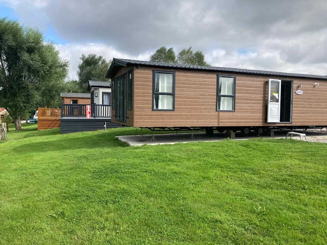 Two static caravans on a grassy area, surrounded by trees under a cloudy sky in Yafforth, Yorkshire.