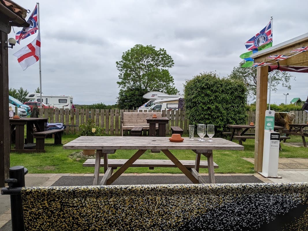 Outdoor seating area at The Providence Inn with picnic tables, flags, and a view of caravans and greenery.