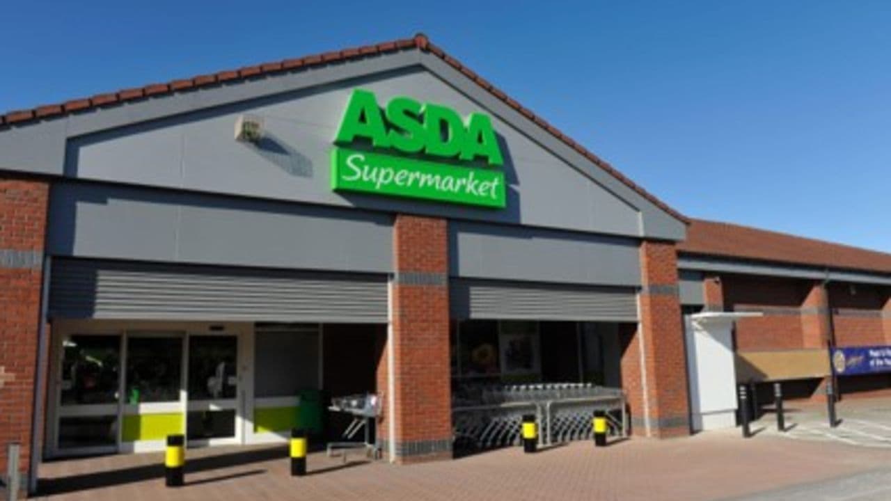 Asda Supermarket storefront with green signage, shopping carts outside, and a clear blue sky above.