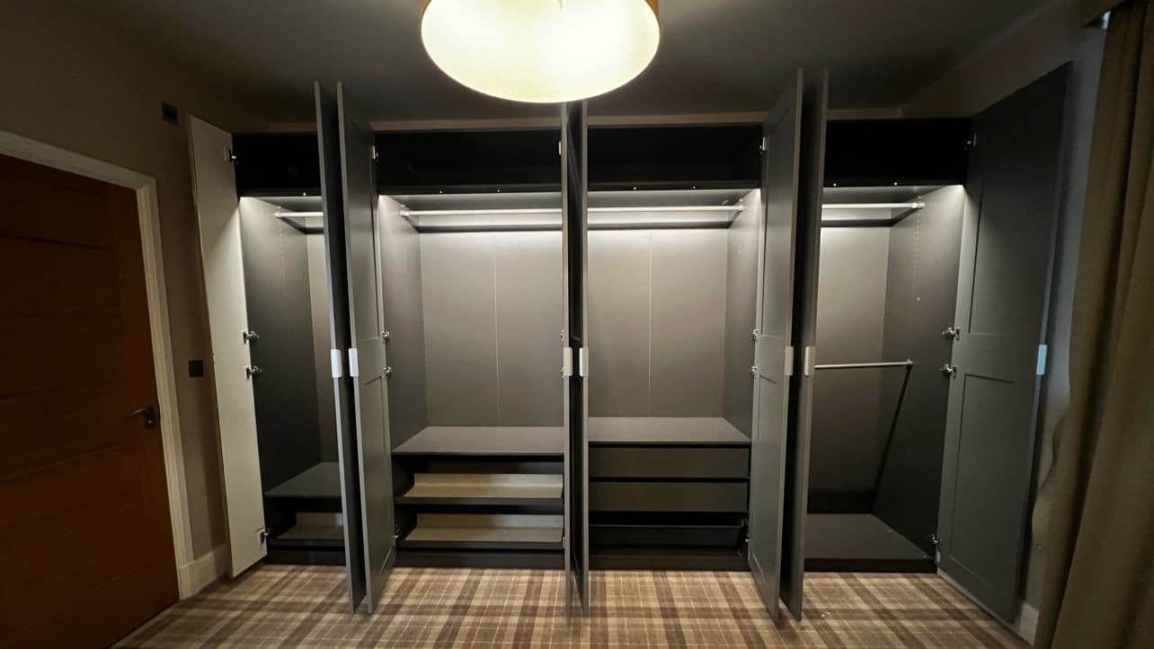 Modern, spacious wardrobe with open doors, built-in lighting, and shelves, set against a neutral wall and patterned floor.