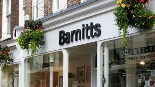 Signage reading "Barnitts" with floral displays hanging above a shopfront in York, Yorkshire.