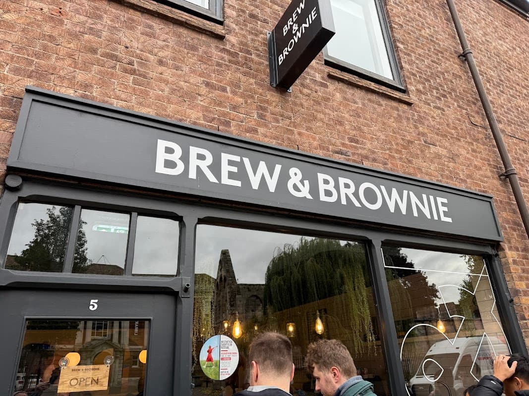 Signage for "Brew & Brownie" cafe on a brick building, with a view of customers outside.