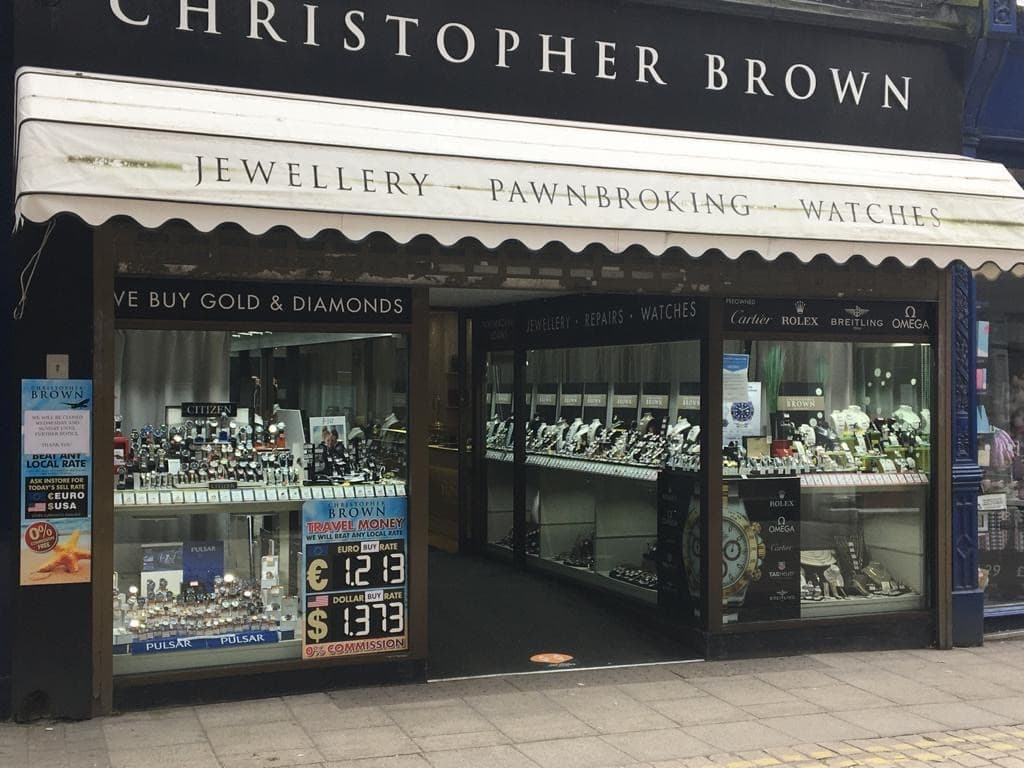 Jewellery shop front featuring displays of watches, gold, and diamonds, with a sign for pawnbroking services.