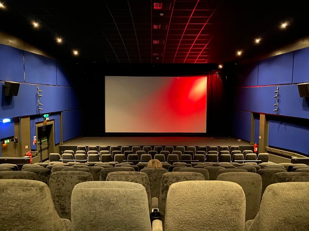 Interior of a theater with plush gray seating, a large screen, and blue walls, illuminated by soft red lighting.