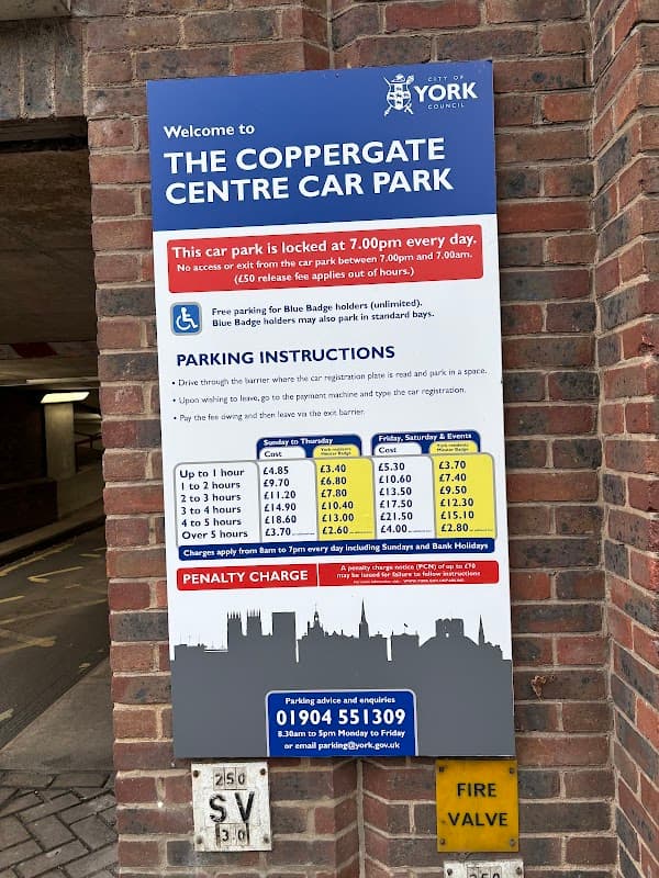 Welcome sign for Coppergate Centre Car Park with parking instructions and fees displayed on a brick wall.