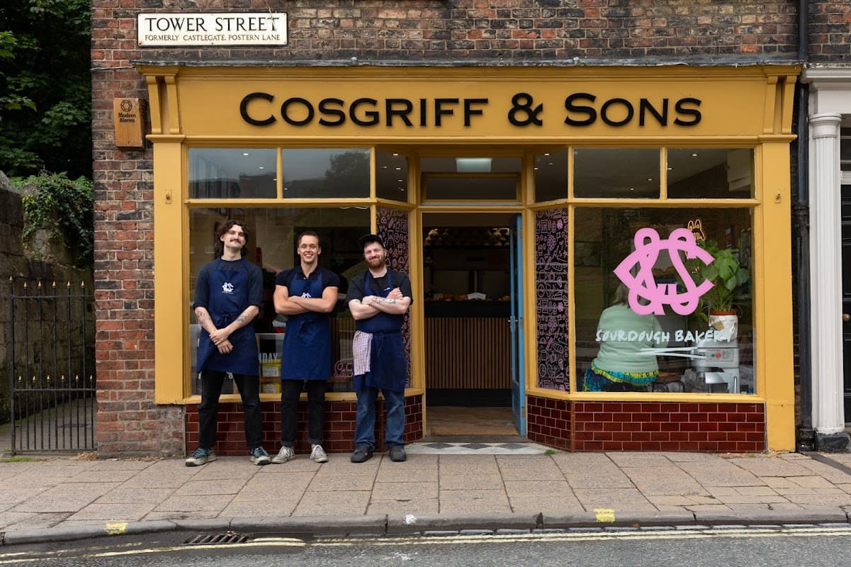 Cosgriff and Sons Microbakery storefront with three bakers in aprons, colorful baked goods visible inside, and brick facade.