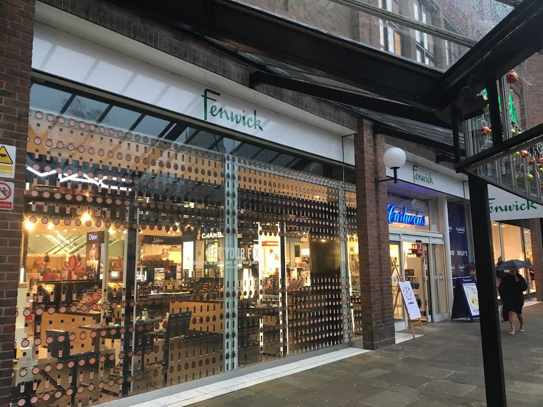 Fenwick store entrance with large glass windows, showcasing displays and signage, in a shopping area in York.