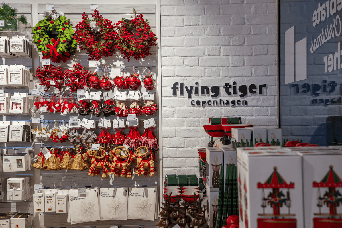 Colorful holiday decorations, including wreaths and ornaments, displayed on a white brick wall at Flying Tiger Copenhagen.