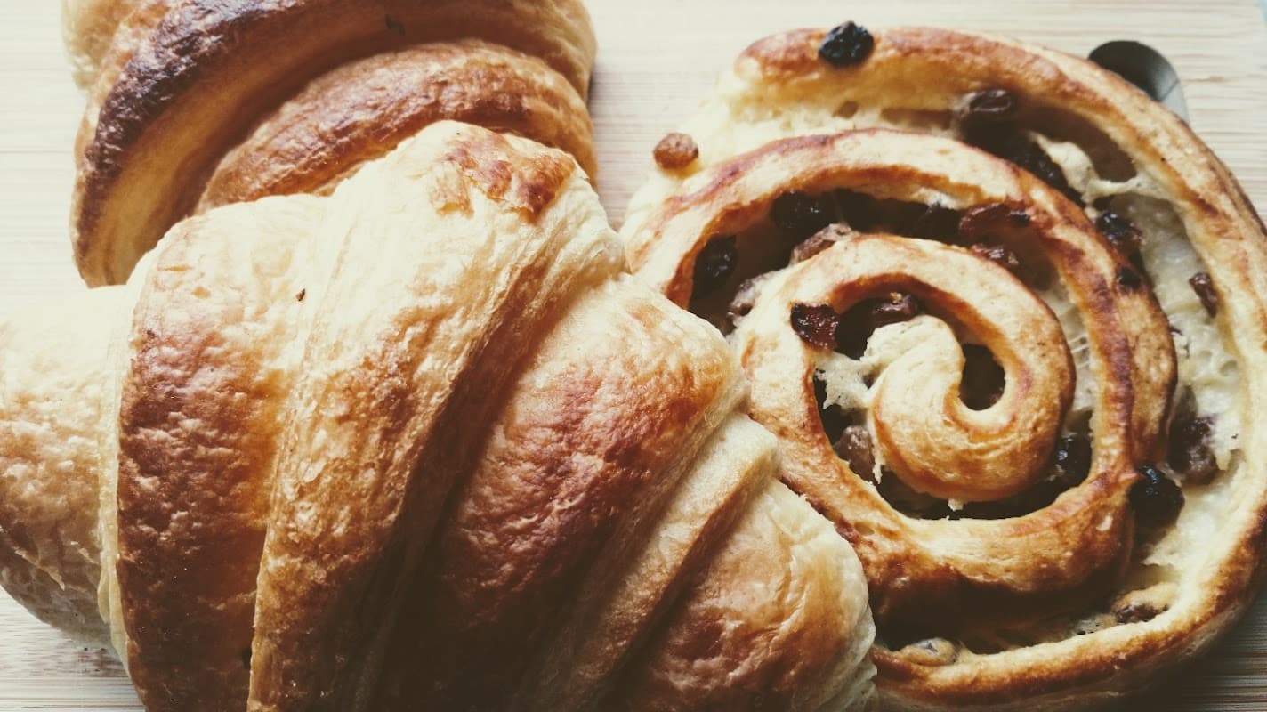 Golden croissants and a cinnamon roll with raisins, freshly baked and resting on a wooden surface.