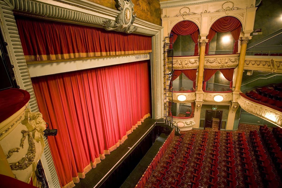 Ornate theater interior featuring a grand red curtain, plush seating, and decorative balconies in the Grand Opera House, York.