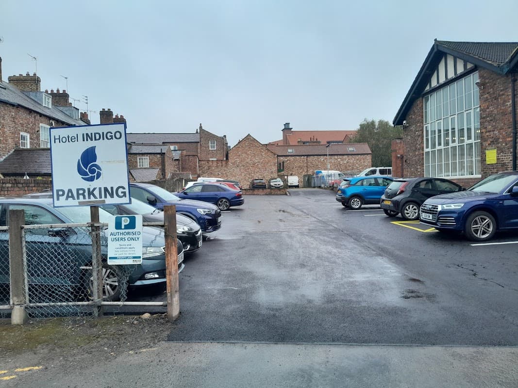 Hotel Indigo car park with several parked cars, a sign indicating parking rules, and brick buildings in the background.