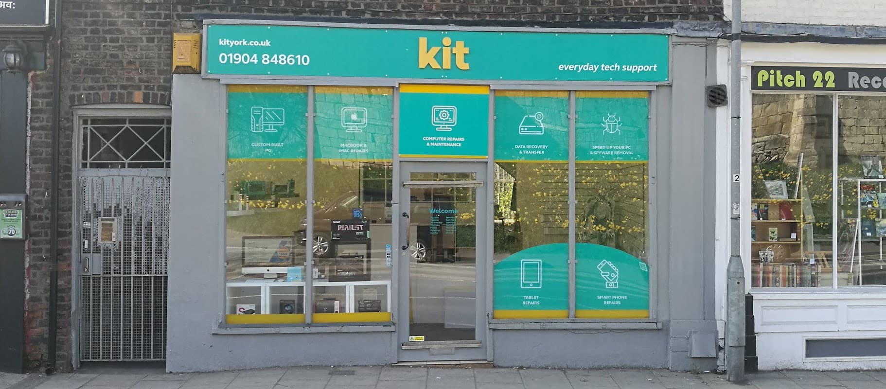 Bright storefront with "kit" signage, displaying tech support services and products behind glass windows.