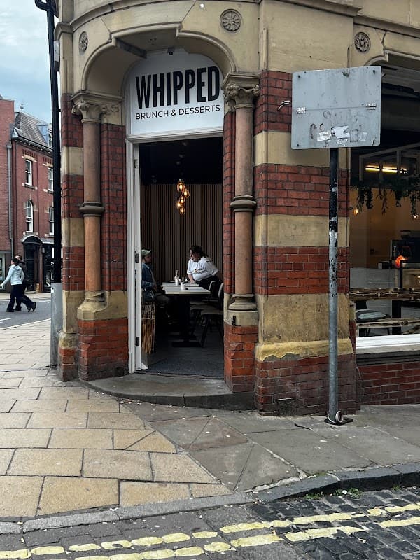 Entrance to Whipped café featuring brick architecture, outdoor seating, and patrons enjoying brunch inside.