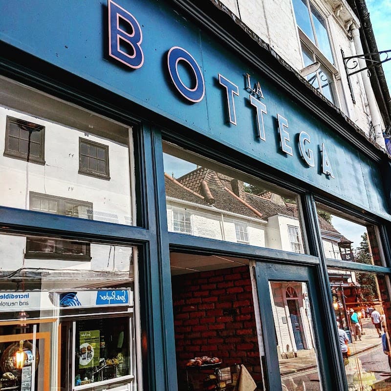 Blue storefront with "La Bottega" sign, large windows reflecting nearby buildings in a charming York street.