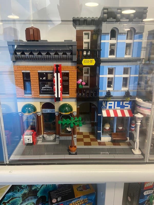 Toy shop display featuring detailed LEGO buildings, including a café and a barber shop, with colorful signage and trees.