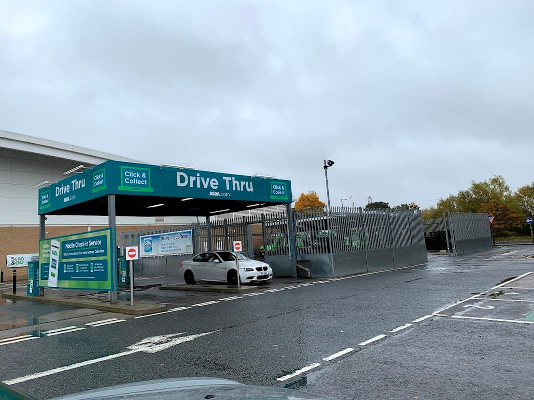Drive-thru sign at Monks Cross North shopping center, with a gray car parked in front under a cloudy sky.