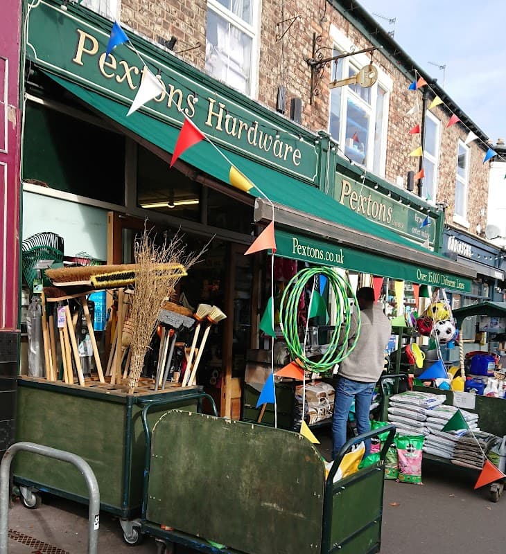 Pextons Hardware storefront with colorful bunting, garden tools, and various supplies displayed outside.