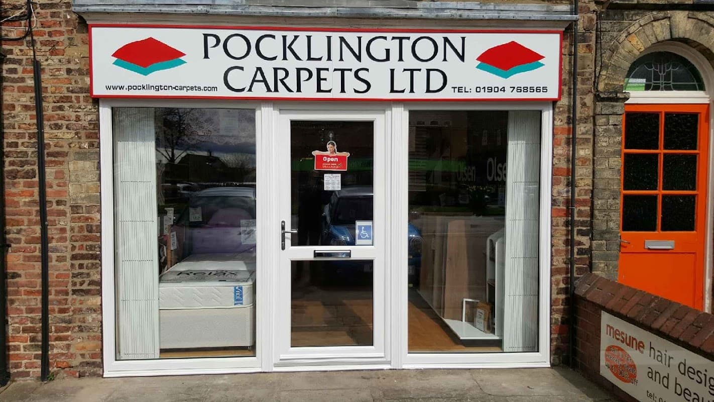 Storefront of Pocklington Carpets Ltd, featuring a white door, large windows, and a red and white sign.