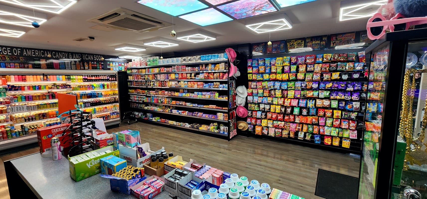 Colorful shelves filled with snacks, drinks, and sweets in a well-lit corner shop, with a vibrant ceiling design.
