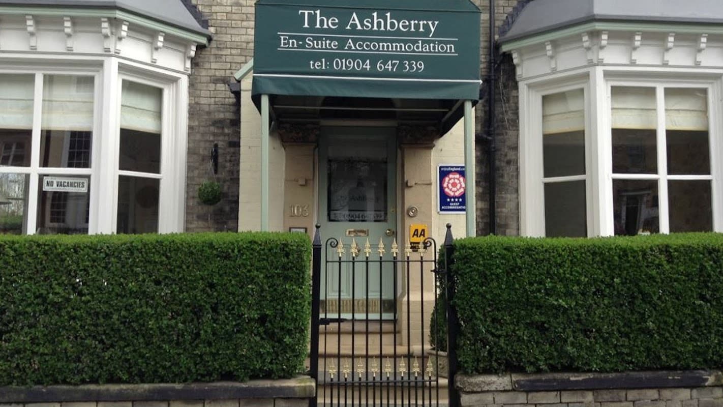 Green awning with "The Ashberry" sign, brick facade, decorative hedges, and a gated entrance in York.