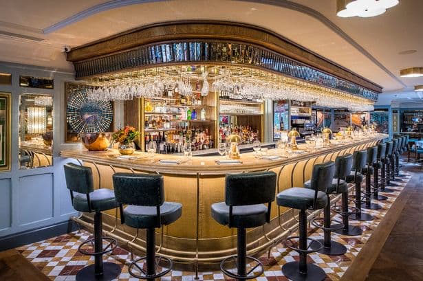 Elegant bar with a curved counter, high stools, glassware, and decorative mirrors in a stylish restaurant setting.