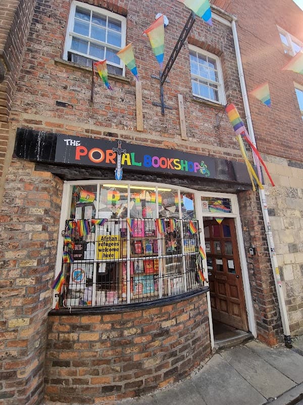 Colorful flags adorn the exterior of The Portal Bookshop, showcasing a vibrant window display of books.