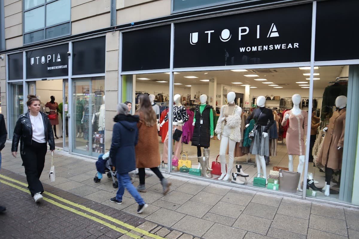 Shopfront of Utopia Womenswear featuring mannequins in stylish clothing, with shoppers walking by on the street.