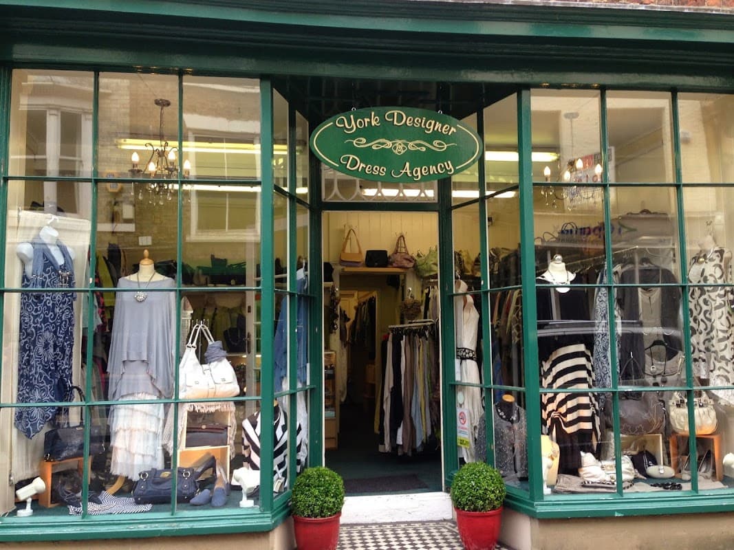 Storefront of York Designer Dress Agency with clothing displays, mannequins, and potted plants at the entrance.