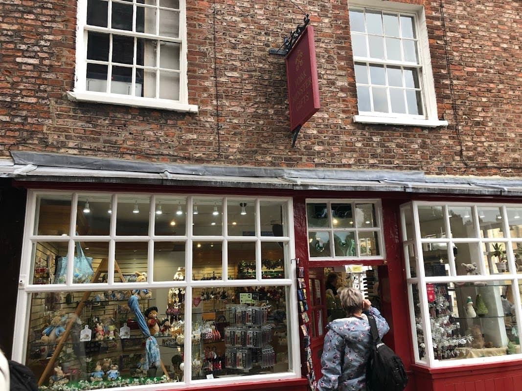 Gift shop with a red storefront, large windows displaying various souvenirs, and a brick wall backdrop.