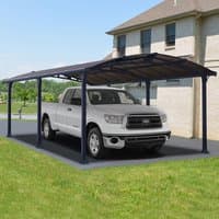 Grey metal carport with arched roof, supported by dark frames, covering a white truck beside a house.