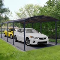 Grey metal carport with arched roof, supported by multiple columns, covering two parked cars on a driveway.