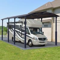 Grey metal carport with arched roof, supported by dark metal beams, covering a large RV next to a house.