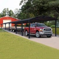 Grey metal carport with arched roof, supported by black columns, covering a driveway with a red truck underneath.