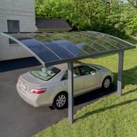 Grey metal carport with curved roof and transparent panels, covering a silver sedan, set on a driveway.